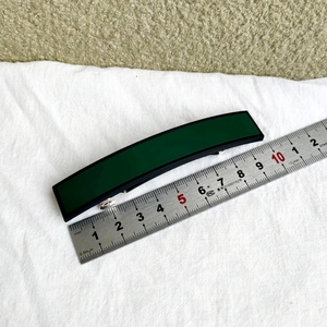 Détail d'une barrette à cheveux rectangulaire vert foncé de 10cm sur tissu blanc