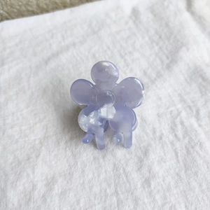 Detail view of a small lavender flower hair claw clip on white textured linen fabric