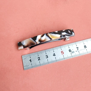 Detail showing an 8cm rectangular marble pattern hair clip being measured on a red fabric