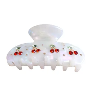 Detailed view of white iridescent cherry hair claw clip with red and green rhinestones