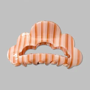 Détail de la pince à cheveux ondulée avec rayures orange et mécanisme à ressort métallique