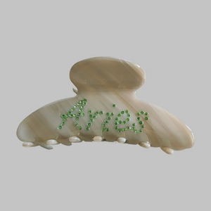 Detail of the hair claw clip showing marble texture and green rhinestone Angels lettering
