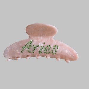 Macro shot of pink marble hair claw clip with Aries lettering in green rhinestones