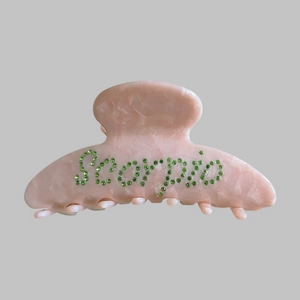 Close-up of pink marble hair claw clip with Scorpio lettering in green rhinestones