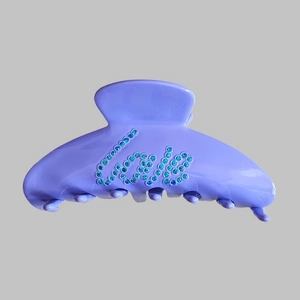 Detail view of purple matte hair claw clip with blue rhinestone cool lettering embellishment