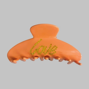 Close-up of orange glossy hair claw clip featuring yellow rhinestone Love letters