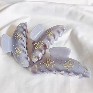 Detail of three taro purple acetate flower hair claws with rhinestone stars on white fabric