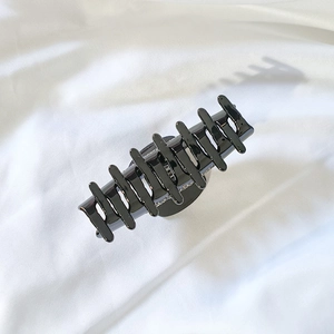 Détail d'une pince à cheveux noire brillante avec design multi-dents sur tissu blanc