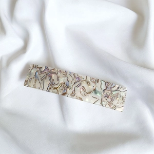 Detailed close-up of a large French acetate hair clip with marble patterns on white silk