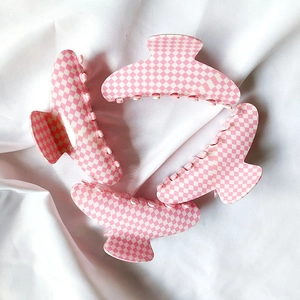 Vue détaillée de quatre pinces à cheveux à damier rose et blanc sur tissu blanc