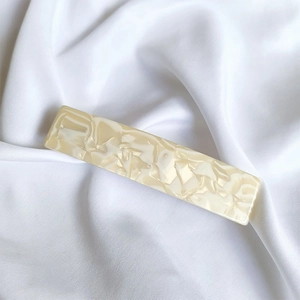 Detail of a large French acetate hair clip with cream marble texture on white silk fabric