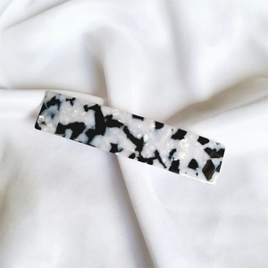 Close-up of a marbled acetate rectangular hair clip on elegant white silk fabric
