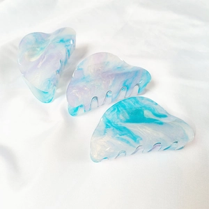 Detail of shimmering blue acrylic hair claws with marble texture and glitter on silk
