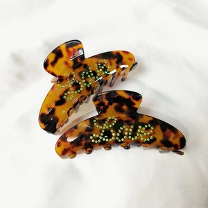Detailed view of acetate hair claw clips with green rhinestone Love lettering