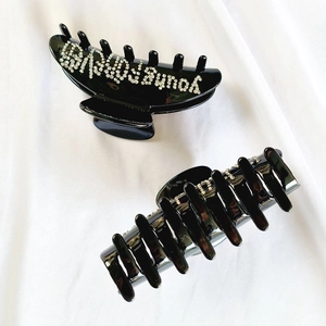 Dettaglio di una grande pinza per capelli nera con decorazione in strass della scritta Young