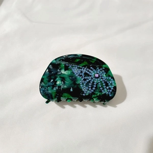 Detail of dark green marbled claw clip featuring a blue rhinestone butterfly motif