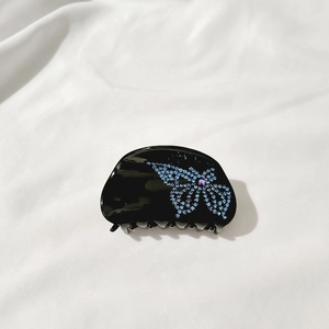 Close-up of black hair claw clip featuring a blue rhinestone butterfly and purple center gem