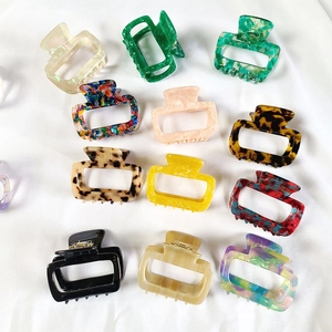 Flat lay showing twelve diverse colors of square acetate hair claws on a soft fabric base