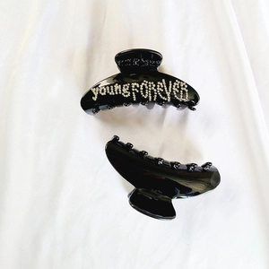 Dettaglio di una pinza per capelli nera con strass bianchi e scritta Young Forever