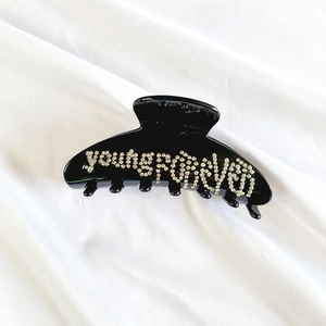 Dettaglio di un fermaglio per capelli nero con scritta young forever in strass bianchi