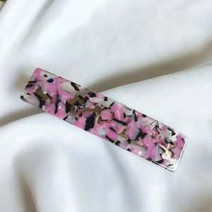 Detail of elegant rectangular acetate hair clip with pink marble pattern on white satin