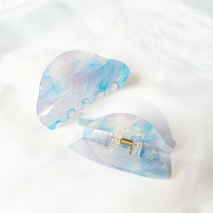 Detail view of two blue-purple marbled acrylic hair claws with gold springs on white fabric