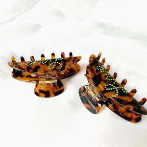 Elegant tortoise shell claw clips with green rhinestone logo on white fabric