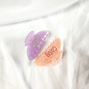 Détail de pinces à cheveux en acétate violet et rose avec lettrage COSY et GOOD strass