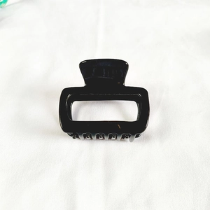 Detailed top view of a glossy black square acetate hair claw clip on white fabric