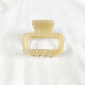 Close-up of a small square acetate hair claw clip in creamy yellow on white fabric