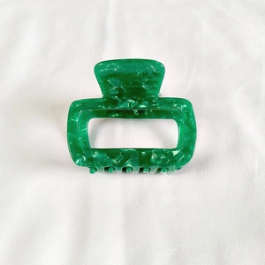 Detail shot of a small green marble pattern acetate hair claw clip on white fabric