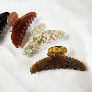 Macro shot of 12cm acetate claw clips in black, amber, and floral patterns on white fabric