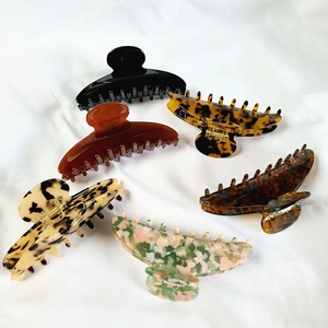 Flat lay of six 12cm acetate claw clips in marble and tortoiseshell patterns on white fabric