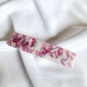 Close-up of pink marble acetate hair clip on white silk fabric background