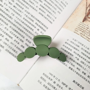Matte bean green large hair claw clip placed on an open book in a lifestyle setting