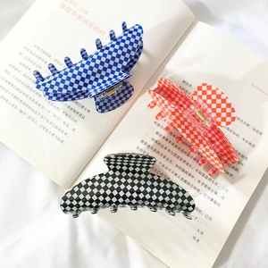 Three large checkered hair claw clips in blue, orange, and black on an open book