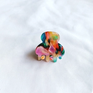 Close-up of a mini acetate hair claw clip with colorful marble pattern on white fabric