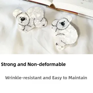 Détail d'une pince à cheveux koala en acétate blanc nacré sur fond de tissu blanc