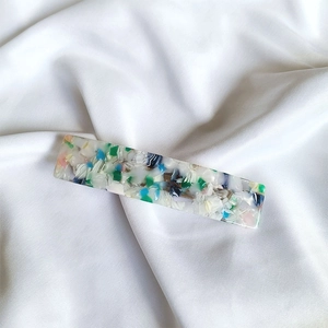 Detailed close-up of a colorful mosaic acetate spring hair clip on white silk fabric