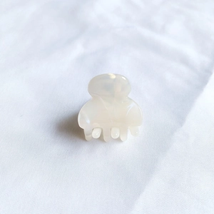 Close-up of a mini cream white acetate hair claw clip on white textured fabric background