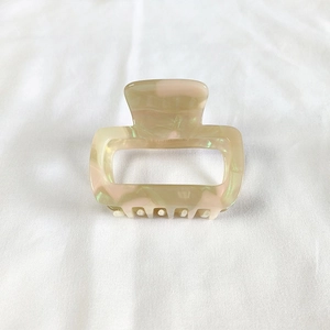 Detail of a square acetate hair claw with pink and green marble texture on white fabric