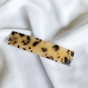 Macro shot of large acetate hair clip with vintage tortoiseshell pattern on white silk fabric