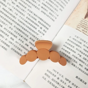 Matte orange large hair claw clip with rounded arcs placed on an open book