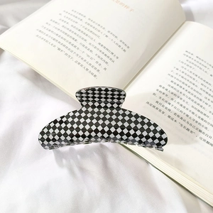 Detailed view of large black and white checkered hair claw clip on white fabric background