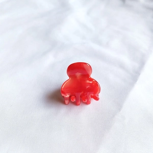 Close-up of a mini red marble acetate hair claw clip on white textured fabric