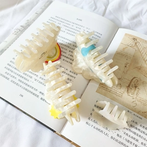 Set of four pearlescent white acetate cloud and sun hair claws on an open book