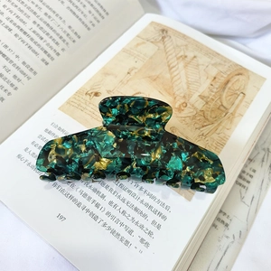 Macro shot of large acetate hair claw clip with vintage green and gold marble texture