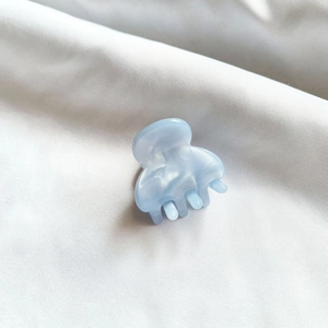 Close-up of a mini light blue acetate hair claw with marble texture on white fabric