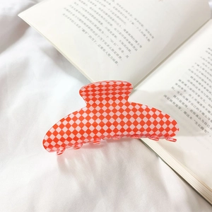 Detail of a large red and white checkered hair claw clip on soft white fabric background