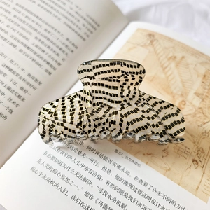 Detailed view of large acetate hair claw clip with black and white checkered pattern on a book